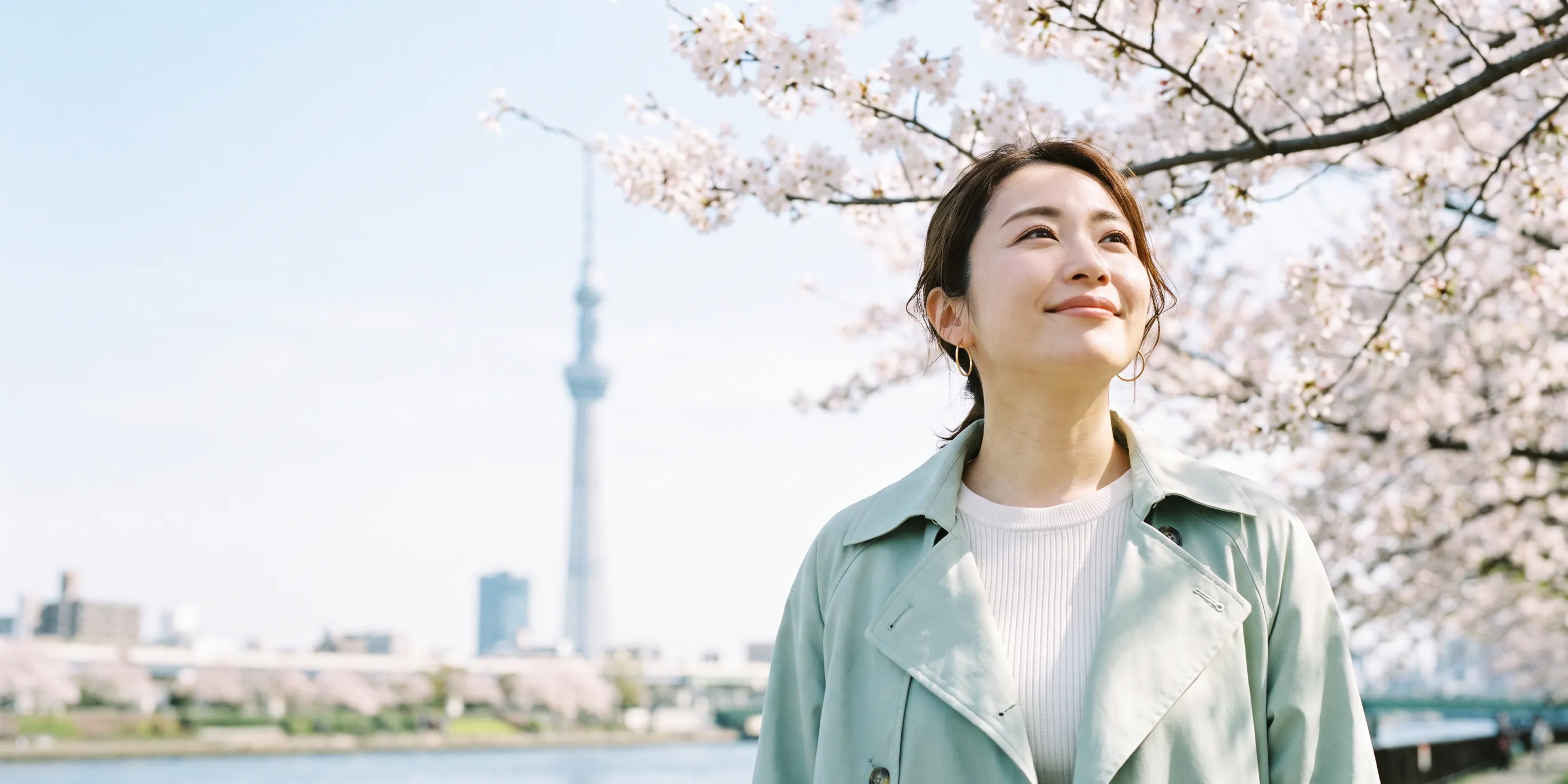 隅田川沿いの桜並木で、桜を見上げて微笑む女性