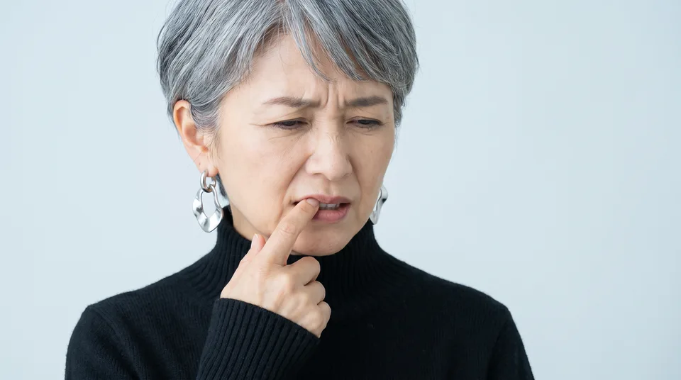 唇の端を指で押さえ、歯ぐきの痛みに困った顔をする女性