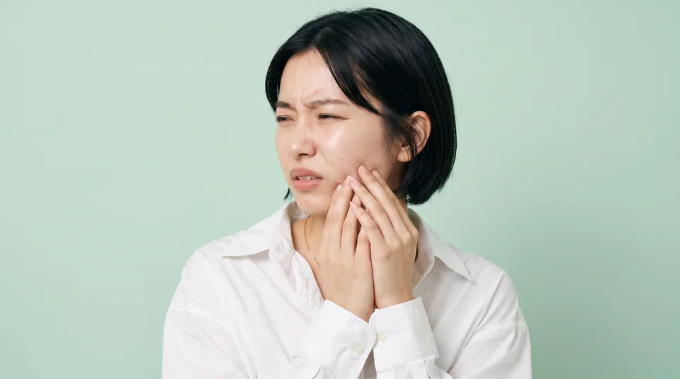 奥歯のあたりの頬を押さえ、痛みに目を細める女性