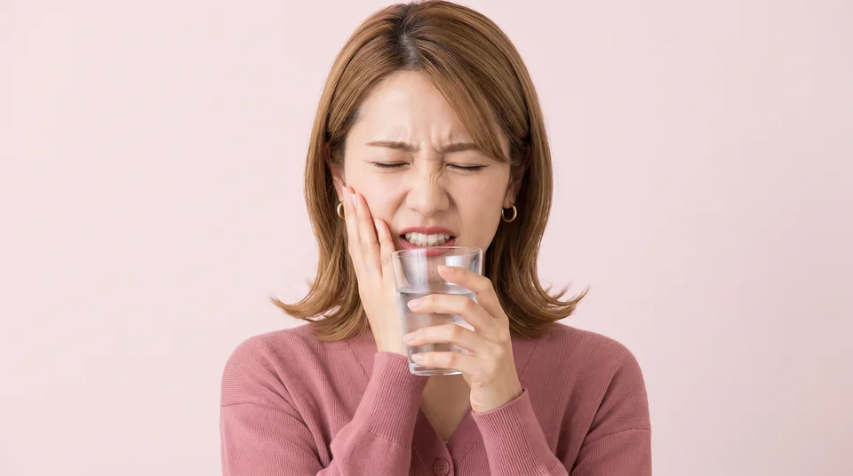 冷たい水のグラスを手に、しみる痛みに頬を押さえる女性